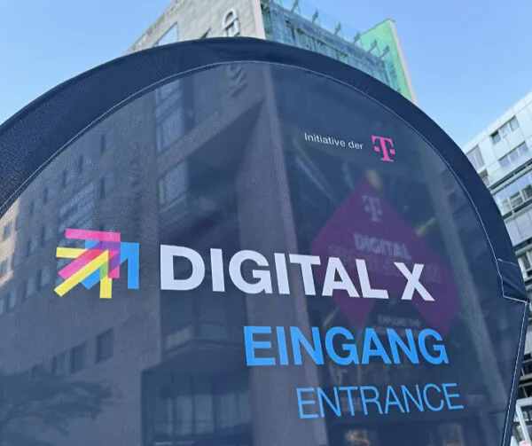 „Schild am Eingang des „Digital X“-Events, einer Initiative der Telekom, vor einem Gebäude.“