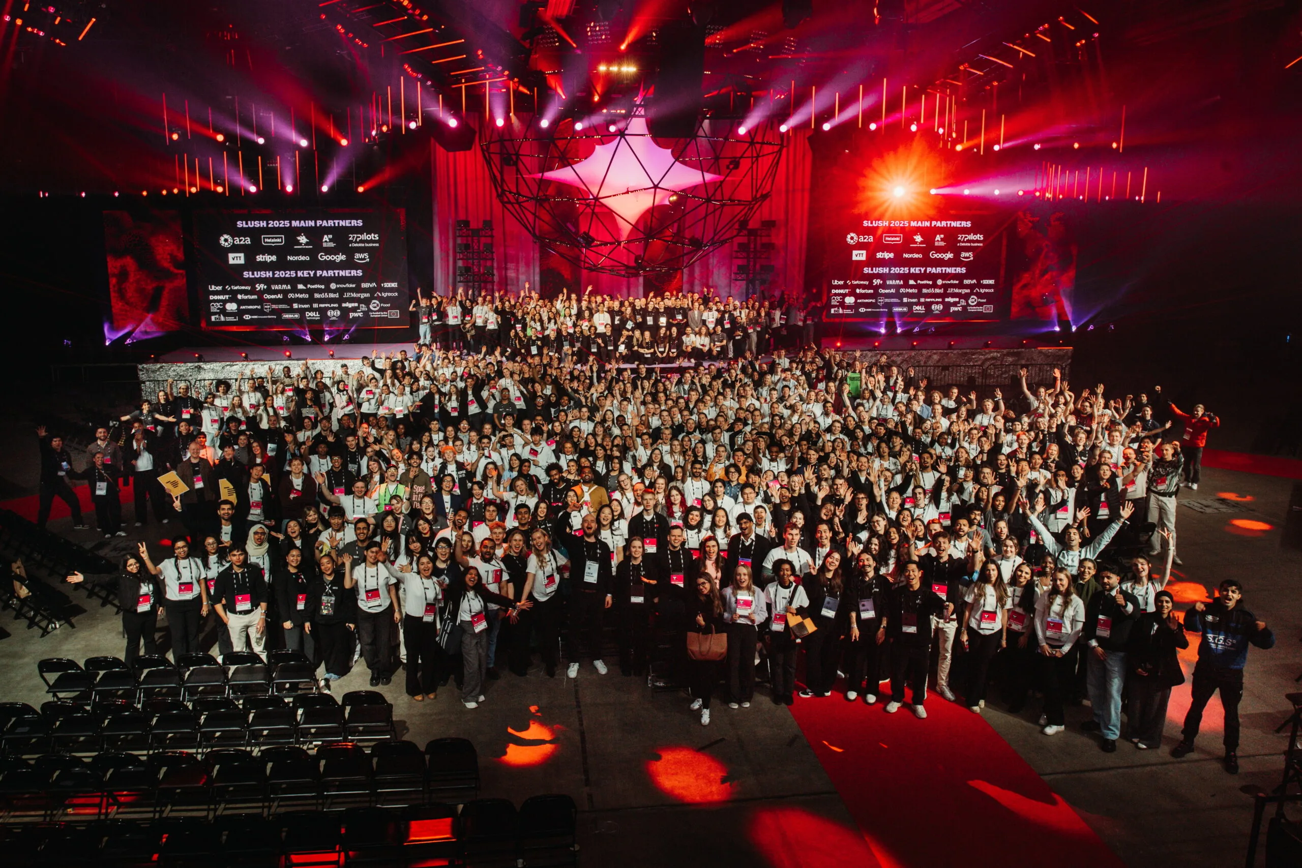 „Großes Gruppenfoto auf der rot beleuchteten Bühne des Slush 2025 Events mit vielen Teilnehmern.“
