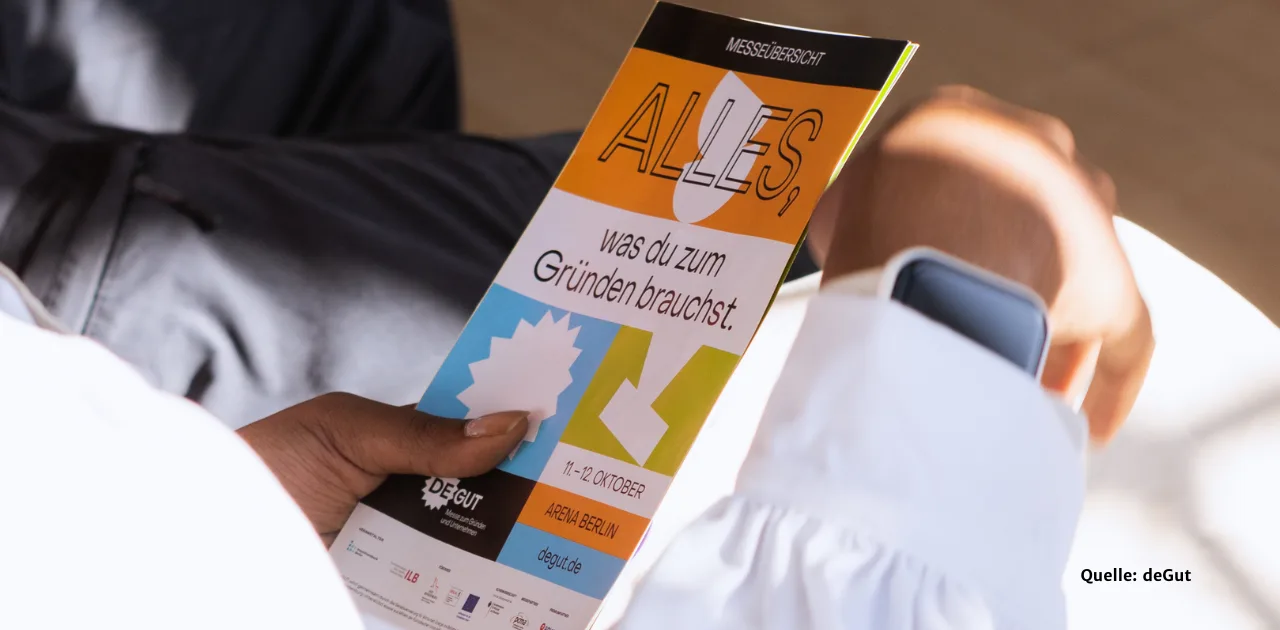 „Eine Person hält einen deGUT-Flyer mit der Aufschrift „ALLES, was du zum Gründen brauchst.“