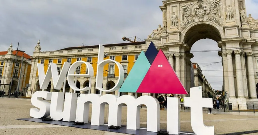 „Großes weißes „Web Summit“-Logo mit bunten Dreiecken vor dem Arco da Rua Augusta in Lissabon.“